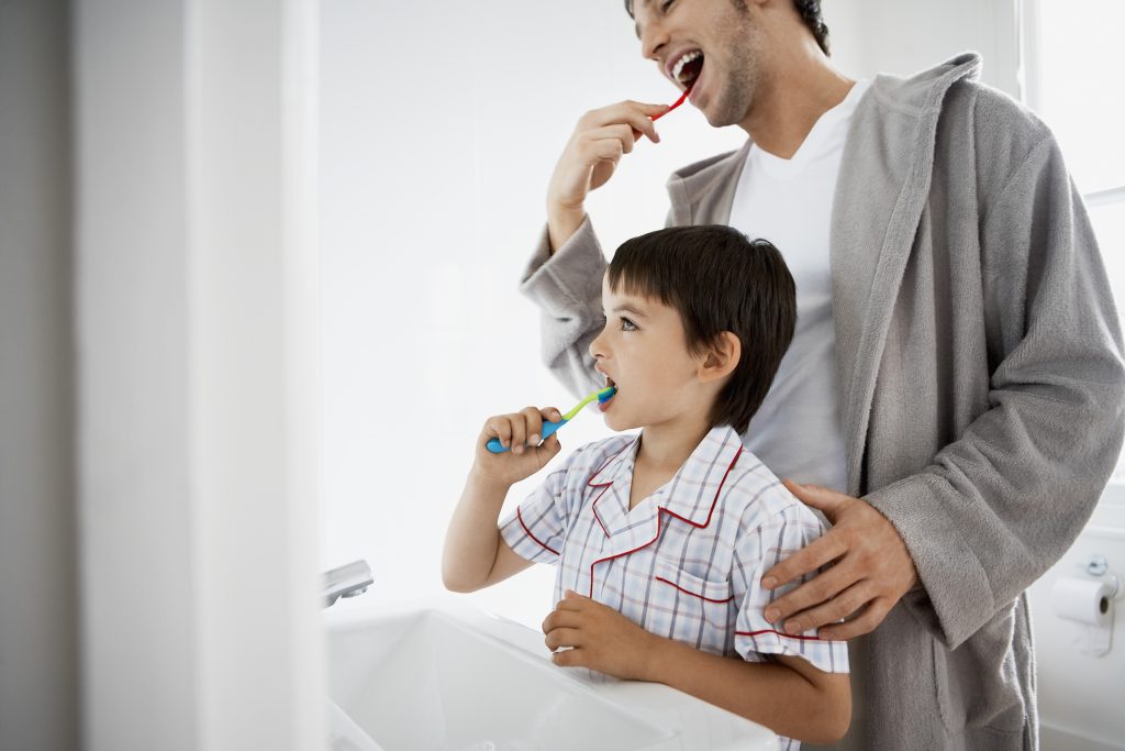 Father helping child brush teeth. 